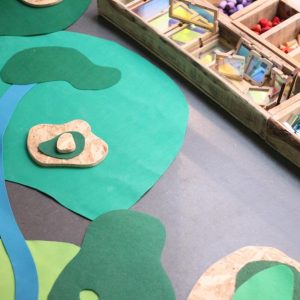Un paisaje de fieltro verde con un río azul junto a los cajones de materiales del taller de piezas sueltas